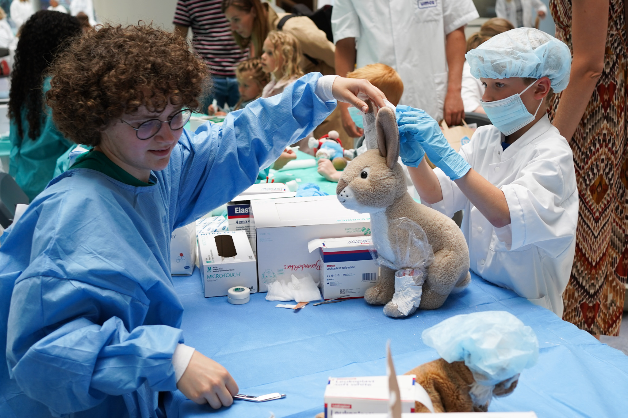 Het oor van een knuffelkonijntje krijgt gips van een jongetje. Een student pakt een schaartje om het gips te knippen.