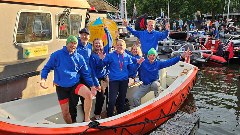 Team 'Operatie te water' bestaat uit 6 UMCG-medewerkers. Allemaal staan ze in een blauwe trui met hun naam in de boot in de Oosterhaven. Deze boot voer mee tijdens de tocht. Ze juichen en zijn blij.