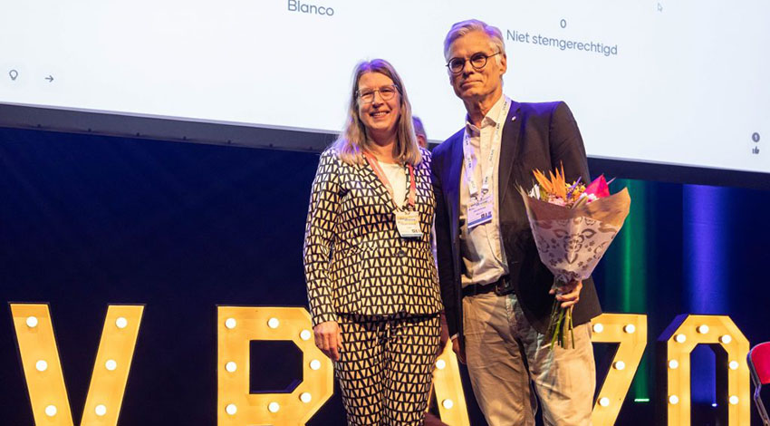 J. Geertzen krijgt uit handen van de voorzitter van de VRA de onderscheiding opgespeld en bloemen overhandigd.