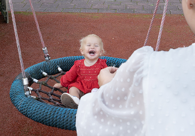 Kira zit lachend op de schommel in een speeltuin van het UMCG.